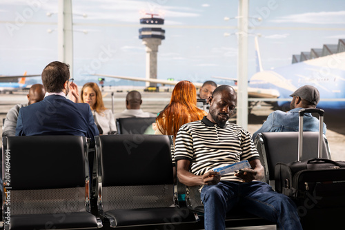 Foto Bored tourists sitting on chairs inside busy airport lounge, waiting for plane to takeoff, diverse travelers enduring tedious waiting for departure during long flight layover, for air travel concepts