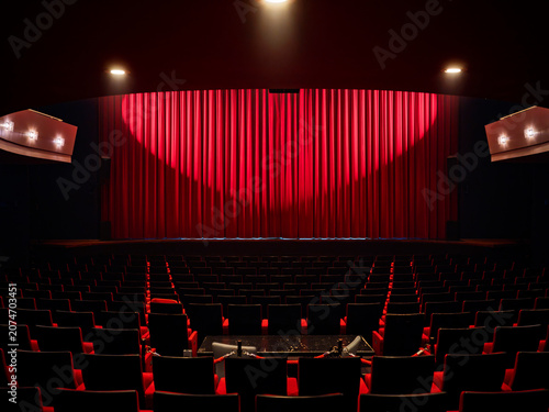 Photography Wide view of an empty theater with a red stage curtain and dark rows of seats, a