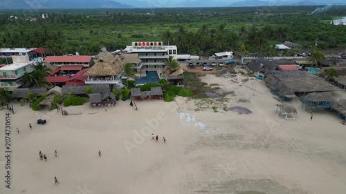 Drone view of Carrizal Beach, Guerrero, Mexico. Hotel and palapa restaurants on sandy shore. People near waves. Tropical nature