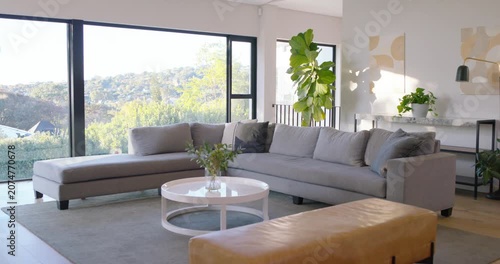 Camera moving right, centering L-shaped gray sofa, showing coffee table, shifting plant shadow