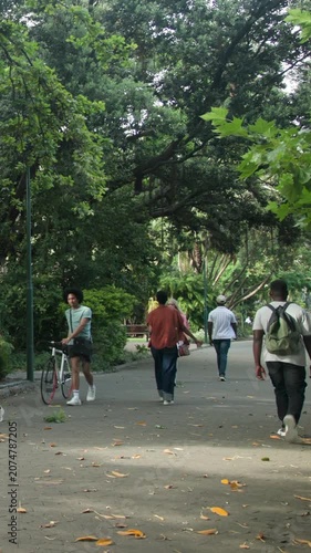 Vertical video: Entering orange-shirted adult walking parkway, passing others with green pack, bike