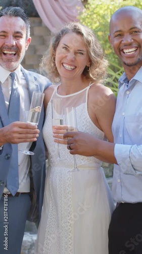 Vertical video: Entering hand clinking flutes, bride in gown raising flute at garden, celebrating