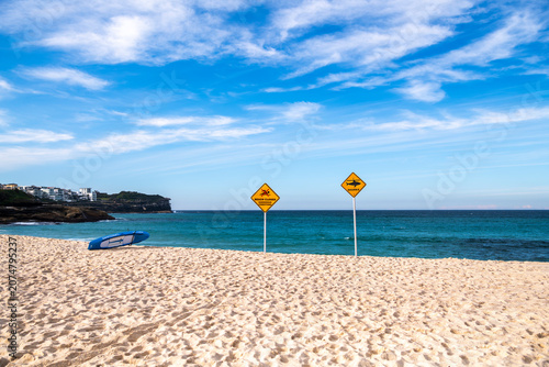 Shark warning and beach closure signs on Bronte Beach following a shark incident, with calm ocean and blue sky, Sydney, Australia.