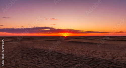 Breathtaking Sunset over a Vast Desert Landscape with Vibrant Orange and Purple Sky