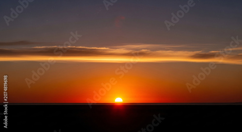 Vibrant Sunset Sky with Brilliant Orange Sun on Horizon and Faint Stars Above Dark Landscape