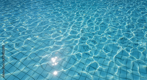 Bright Blue Swimming Pool Water with Sun Reflections and Geometric Tile Patterns on the Bottom