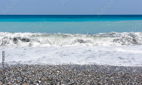 Pacific Ocean waves crashing on a pebble beach in Hualien, Taiwan. Clear blue sky over the coastal landscape. Natural scenery at the shore.