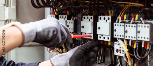 Photos Close-up of electrician hands installing and testing electrical circuit breaker in control panel