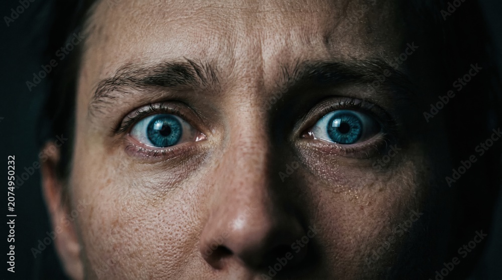 Naklejka premium Close-up portrait of a woman with wide blue eyes looking at the camera with a fearful and anxious expression, portrait