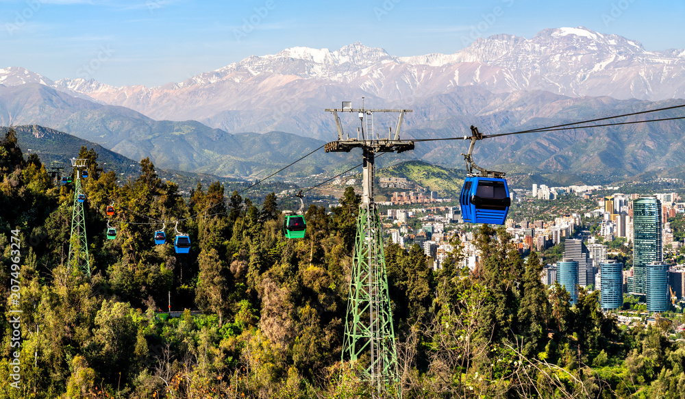 Fototapeta premium Cable cars of Teleferico Santiago glide over Santiago Metropolitan Park with the Andes mountains and city skyline in the distance.