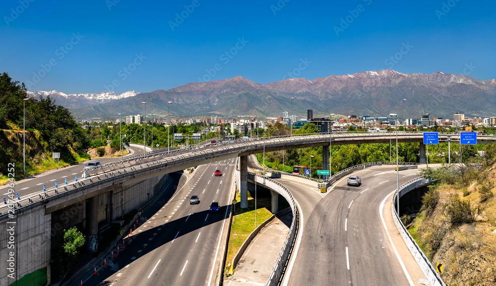 Fototapeta premium Modern highway interchange with traffic and the snow-capped Andes mountains in Santiago, Chile.