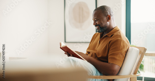 Foto Reading, relax and smile of black man on chair in home living room for fable or fiction