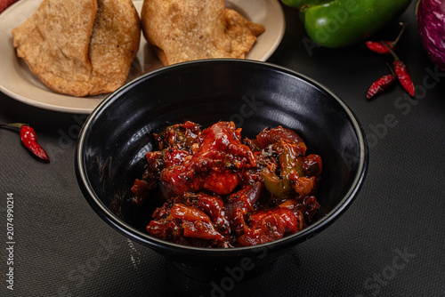 Photos Spicy chicken curry in black bowl with fried bread and red chilies on dark surfa