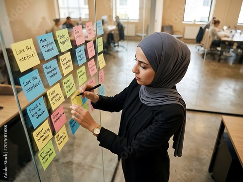 Woman organizing colorful sticky notes on glass wall.