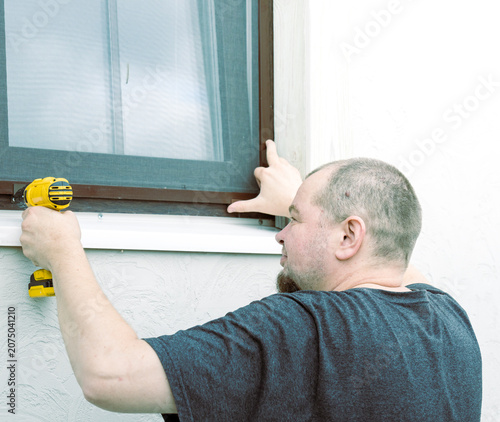 Man installs window screen with power drill