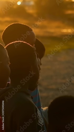 Vertical video: Soccer ball entering drawing boys in hoodie turning heads on dusty lot at sunset