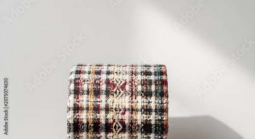 Close-up of a rolled-up colorful woven fabric with a detailed pattern against a white background
