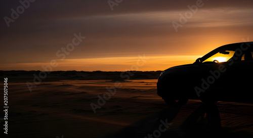 Silhouette of a car parked on a sandy beach at sunset, with the sun setting in the background and a beautiful sky