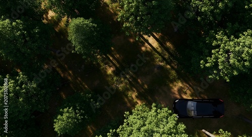 Aerial view of a black car driving on a forest road with trees and shadows during the day