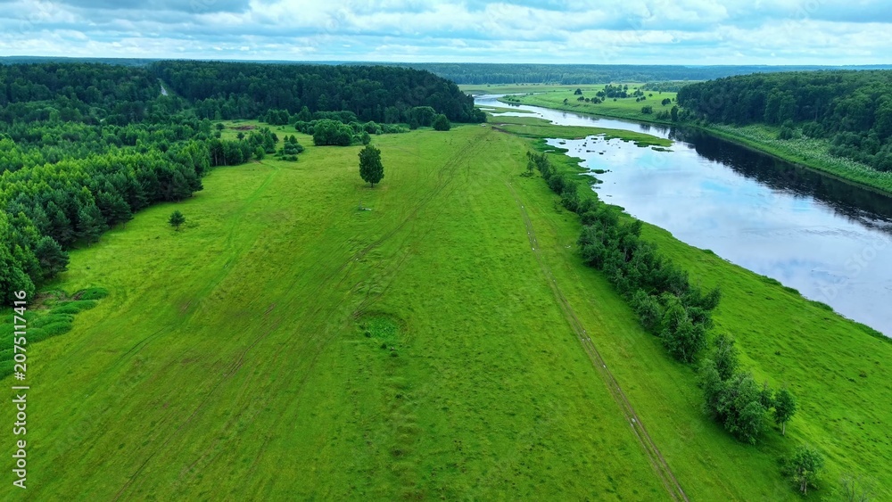 Obraz premium Vibrant lush green fields and winding river under cloudy skies in serene landscape view