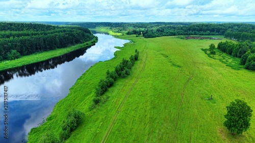 Photos Lush green fields adjacent to a calm river reflecting cloudy skies and trees in