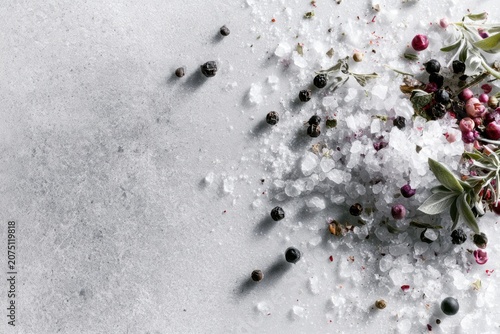 Natural sea salt crystals combined with fragrant herbs and colorful peppercorns creating a clean culinary frame with spacious copy area on a gray background.