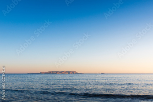 Scenic view of the calm Mediterranean sea surface with the uninhabited island of Dia on the horizon under a clear blue sky in Crete, Greece