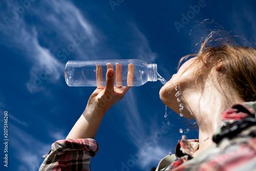 Fotografia Low angle view of a female traveler quenching her thirst by drinking water flowing down her skin under a bright blue sky
