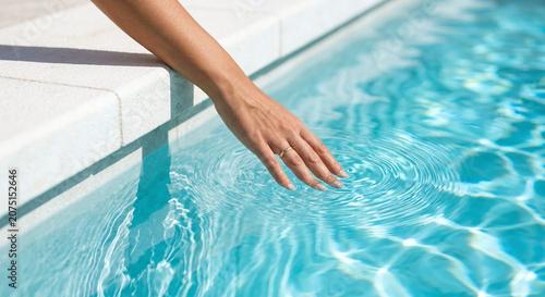 Hand touching crystal clear turquoise swimming pool water in minimalist luxury setting