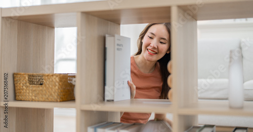 Asian woman shelf bookcase home smiling storage interior organization woman arranging item on wooden furniture in bright living room