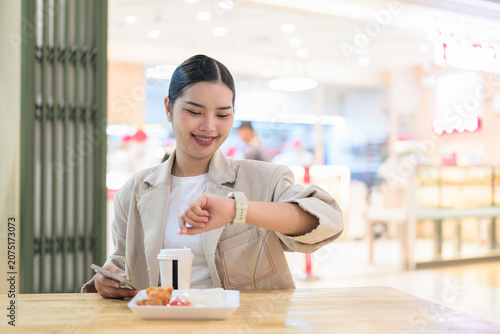 Smiling young Thai Isan businesswoman checking her smartwatch during lunch break