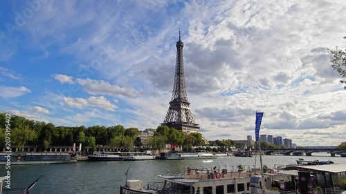 Eiffel Tower viewed from Seine riverbank on a cloudy day, with boats and trees in Paris