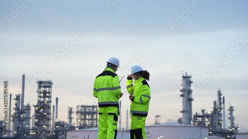 Engineers reviewing plans at oil refinery, Technicians inspecting oil refinery plant at sunset, Oil and gas industry workers team using digital tablet for conducting site survey at petrochemical plant