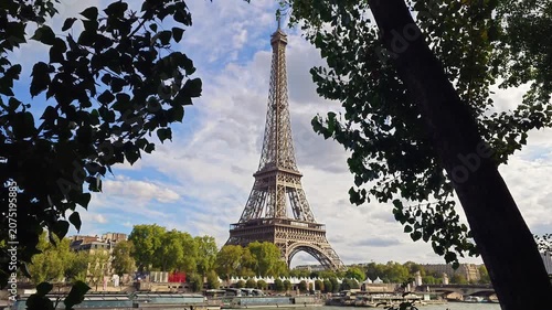 A scenic view of the Eiffel Tower framed by green tree leaves under a cloudy sky in the French capital