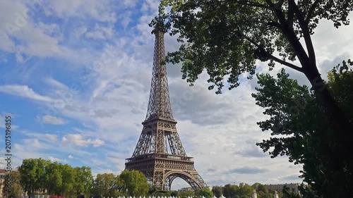 A scenic view of the Eiffel Tower framed by green tree leaves under a cloudy sky in the French capital
