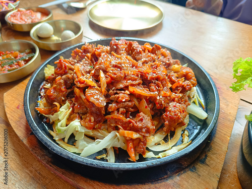 plate of spicy Korean stir-fried meat served on a hot sizzling plate with fresh cabbage and onions, topped with sesame seeds.showcasing authentic Korean cuisine.