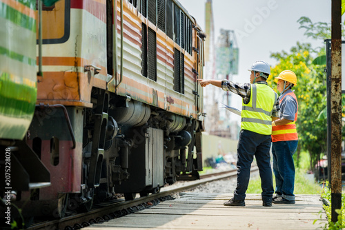 Engineers inspecting a used train car on railway tracks. Professionals in safety gear assess train condition and surrounding construction, highlighting rail maintenance and infrastructure development.