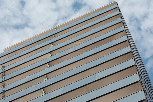 Low angle view of modern high-rise building facade with glass balconies against cloudy sky
