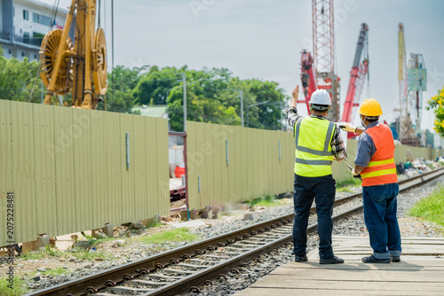 Engineers overseeing track works at a railway construction site. Professionals in safety gear point towards urban infrastructure development, emphasizing project management and progress.