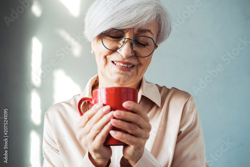 Elderly smiling fashionable happy blonde caucasian woman hold a mug of coffee