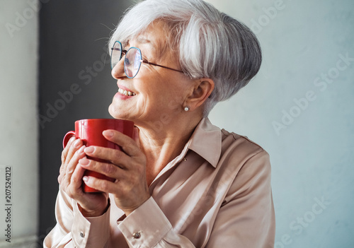 Elderly smiling fashionable happy blonde caucasian woman hold a mug of coffee