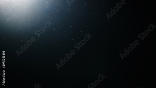 dust particles floating mid air over dark background with some lens flare
