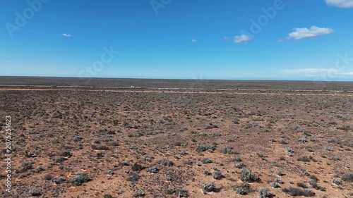 Aerial drone shot flying low over the barren Nullarbor Plain and rising to cross the straight road stretching through the wilderness