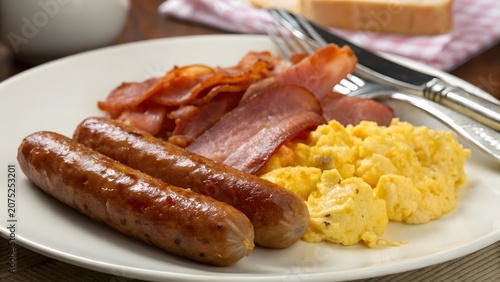 Fresh homemade breakfast featuring juicy sausages golden scrambled eggs and crispy bacon arranged beautifully on a plate