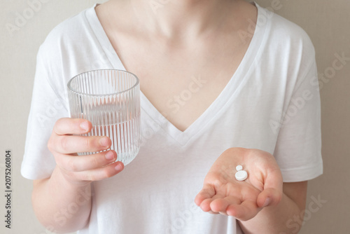 Girl is ill and stay at home. Woman holding pill and glass with water in the hands.