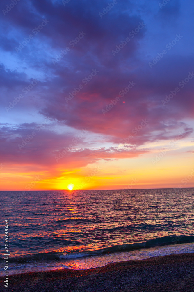 Obraz premium Colorful sunset sea dramatic clouds reflecting vibrant orange, pink purple hues across calm water surface