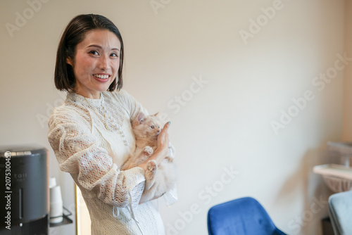 Warm smile meets gentle embrace of a small cat. Soft lace sleeves frame tender, caring gesture. Simple room, quiet moments, calm indoor atmosphere. Cat's quiet trust reflects human warmth