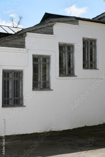 The white wall of a medieval monastery building with four windows with wooden frames arranged in steps
