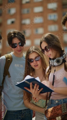 A group of happy young students read a book together while outdoors. Friends collaborate on their studies and share ideas in an urban setting.