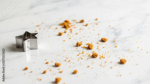 Metal star cookie cutter resting on a white marble surface with scattered brown sugar granules creating a rustic baking preparation scene with soft light